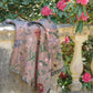 dusky pink woven wrap with bees, butterflies and flowers design draped over stone wall in summer garden