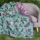 Jade woven blanket spread over sofa in garden with red squirrel, oak, butterflies and birds pattern