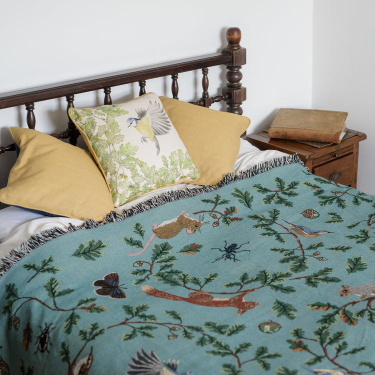 Jade woven blanket spread across bed with red squirrel, oak, butterflies and birds pattern