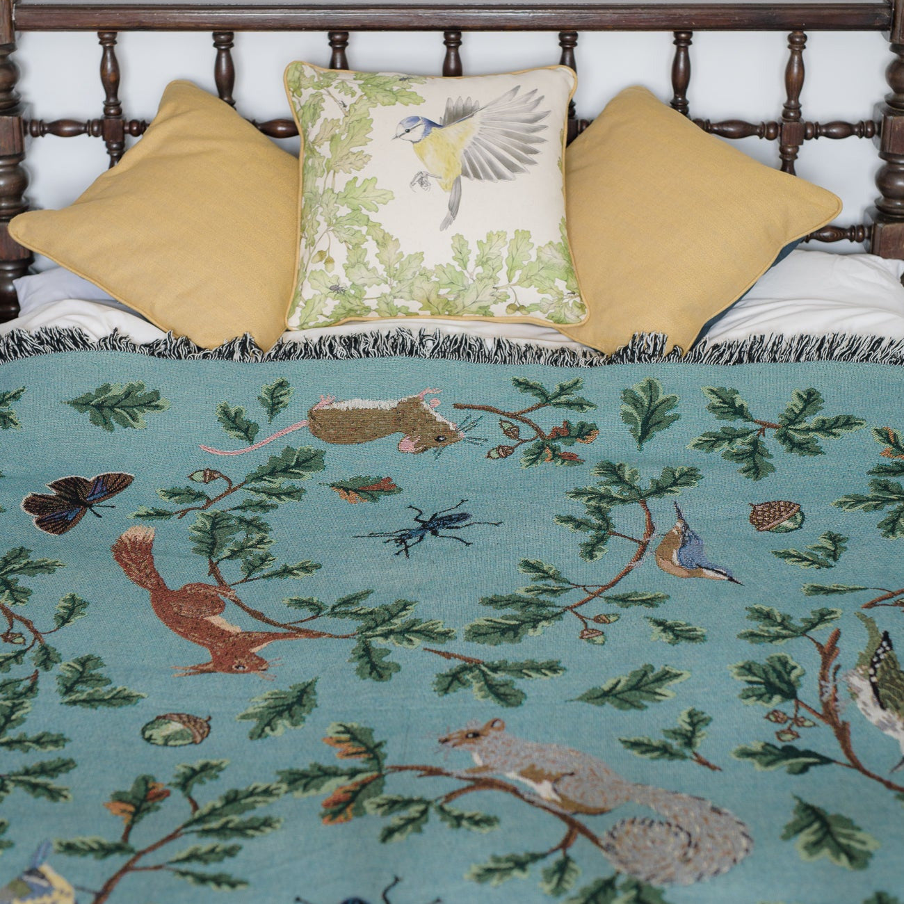 Jade woven blanket spread across bed with red squirrel, oak, butterflies and birds pattern
