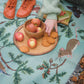 Jade woven picnic blanket spread across forest floor with wood mouse, oak and butterflies pattern with plate of biscuits