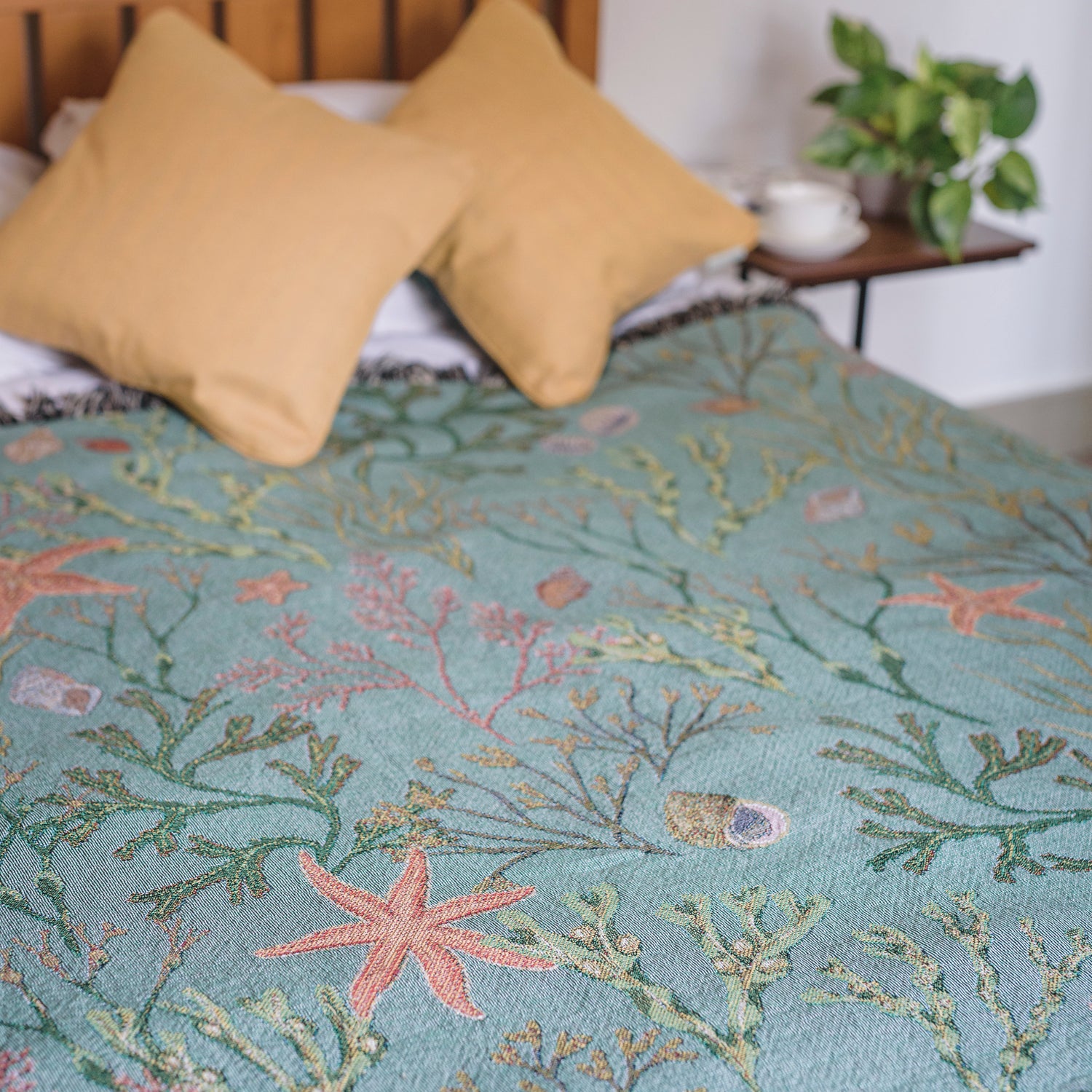 A bed with an Intertidal Star blanket and Arcana pillows on it.