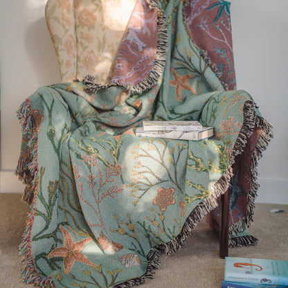 A chair with an Intertidal Star blanket fetauring sea stars and coral and an Arcana book on it.