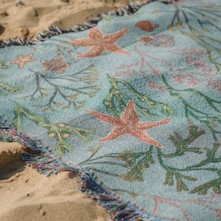 An Arcana Intertidal Star blanket with starfish and seaweed on the sand.