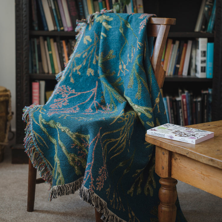 Woven blanket with fringe with delicate seaweed design in blue, green and pink