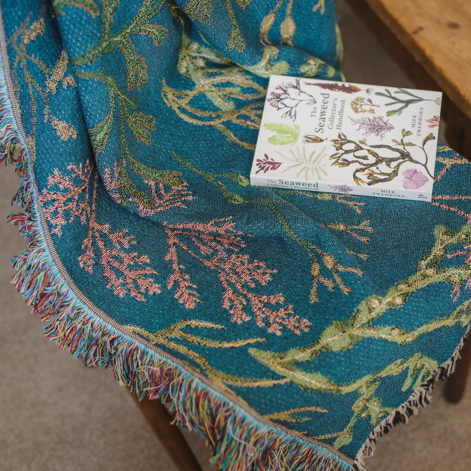 Woven blanket with fringe on chair  with delicate seaweed design in blue, green and pink