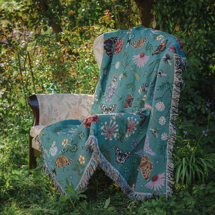 pollination bloom blanket from arcana draped over armchair in a summer garden