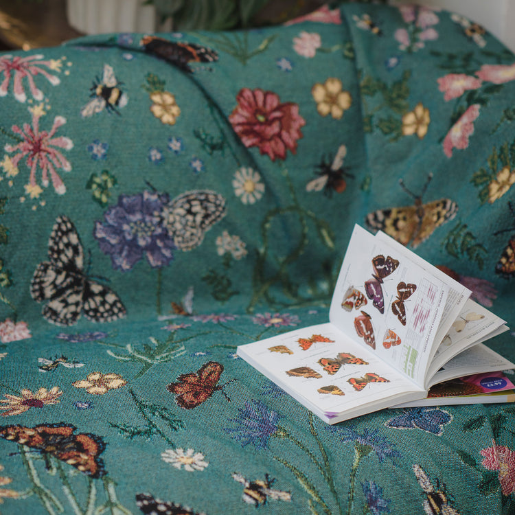 woven throw in teal with butterflies and flowers, thrown over sofa with butterfly book