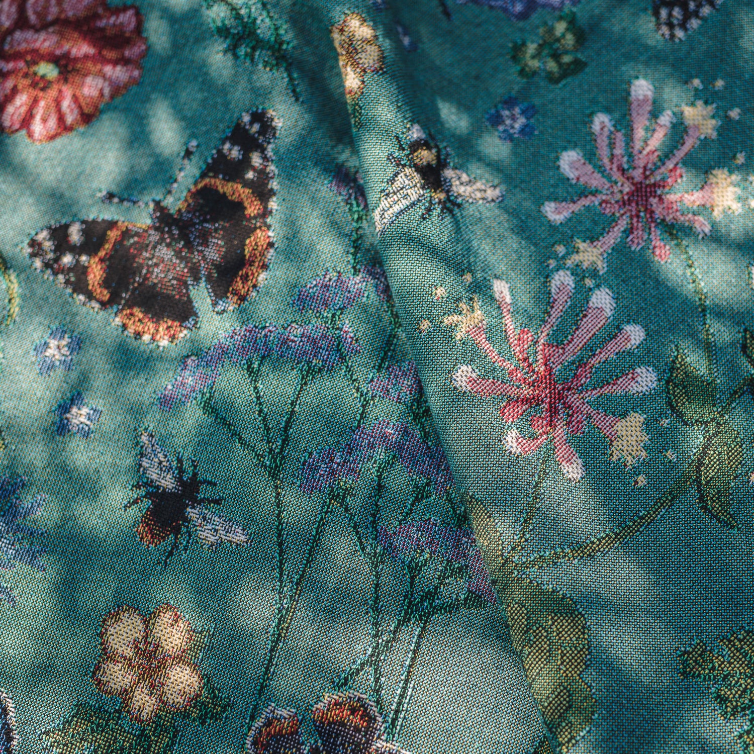 butterfly and flower details on woven green blanket in dappled sunlight