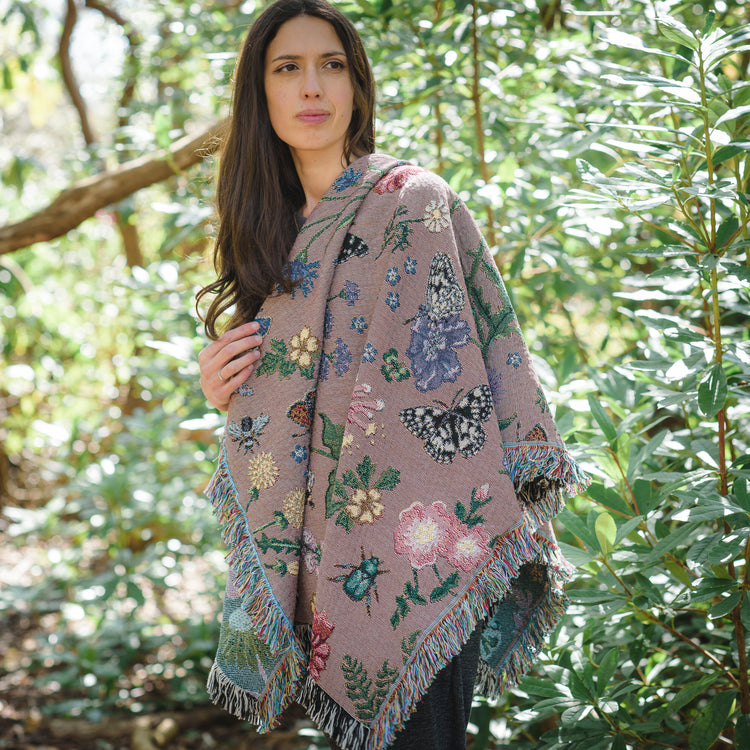 dusky pink woven wrap with bees, butterflies and flowers design wrapped around womans shoulders in woodland