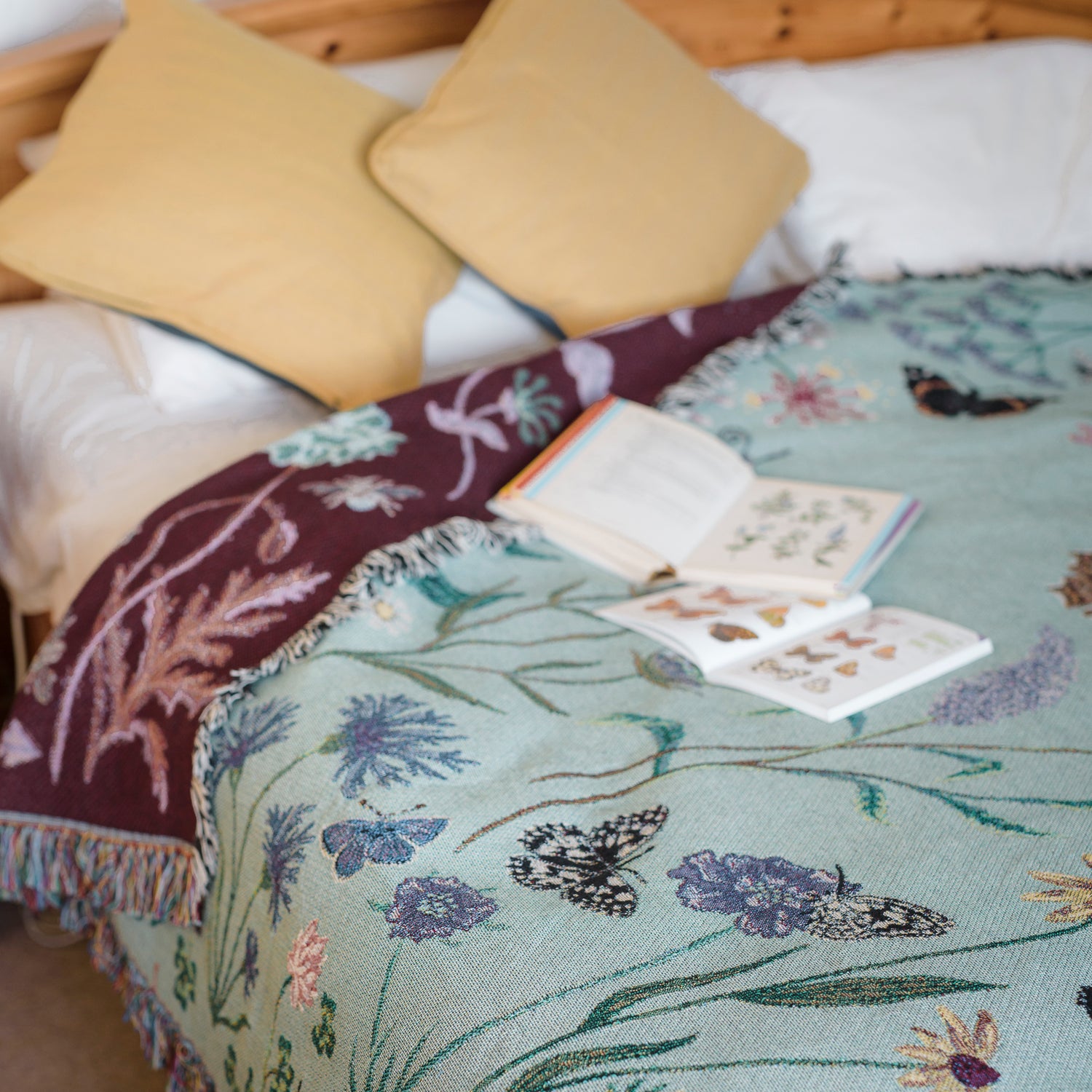 sage green woven blanket with butterflies and wildflowers covering a bed with gold cushions
