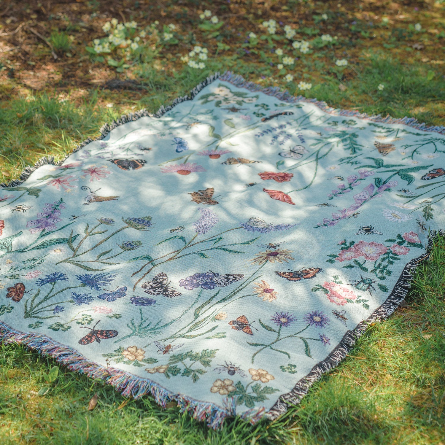 pale green woven picnic blanket in dappled sunlight with wildflower and butterfly pattern