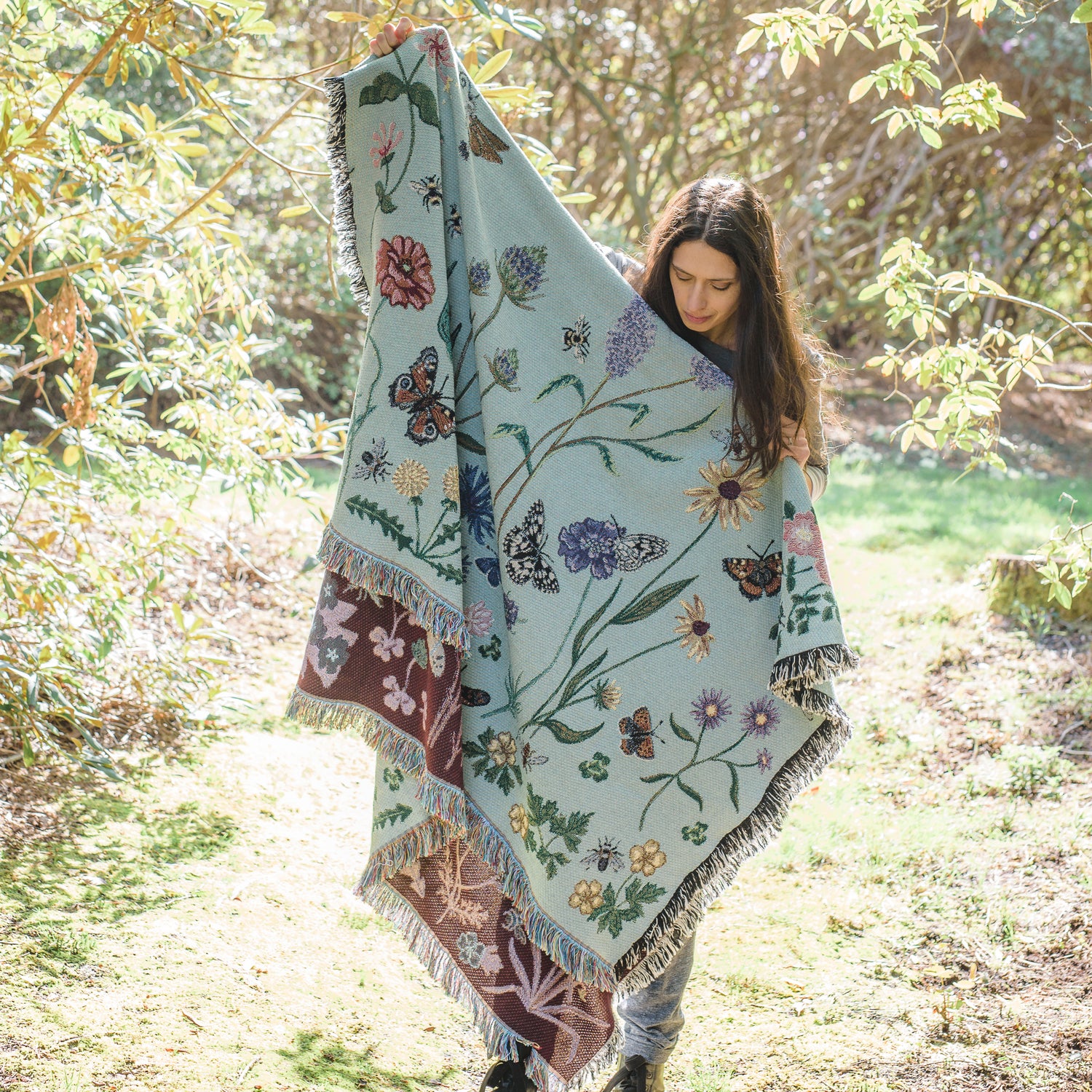 pale green woven blanket held up by woman in dappled sunlight with wildflower and butterfly pattern