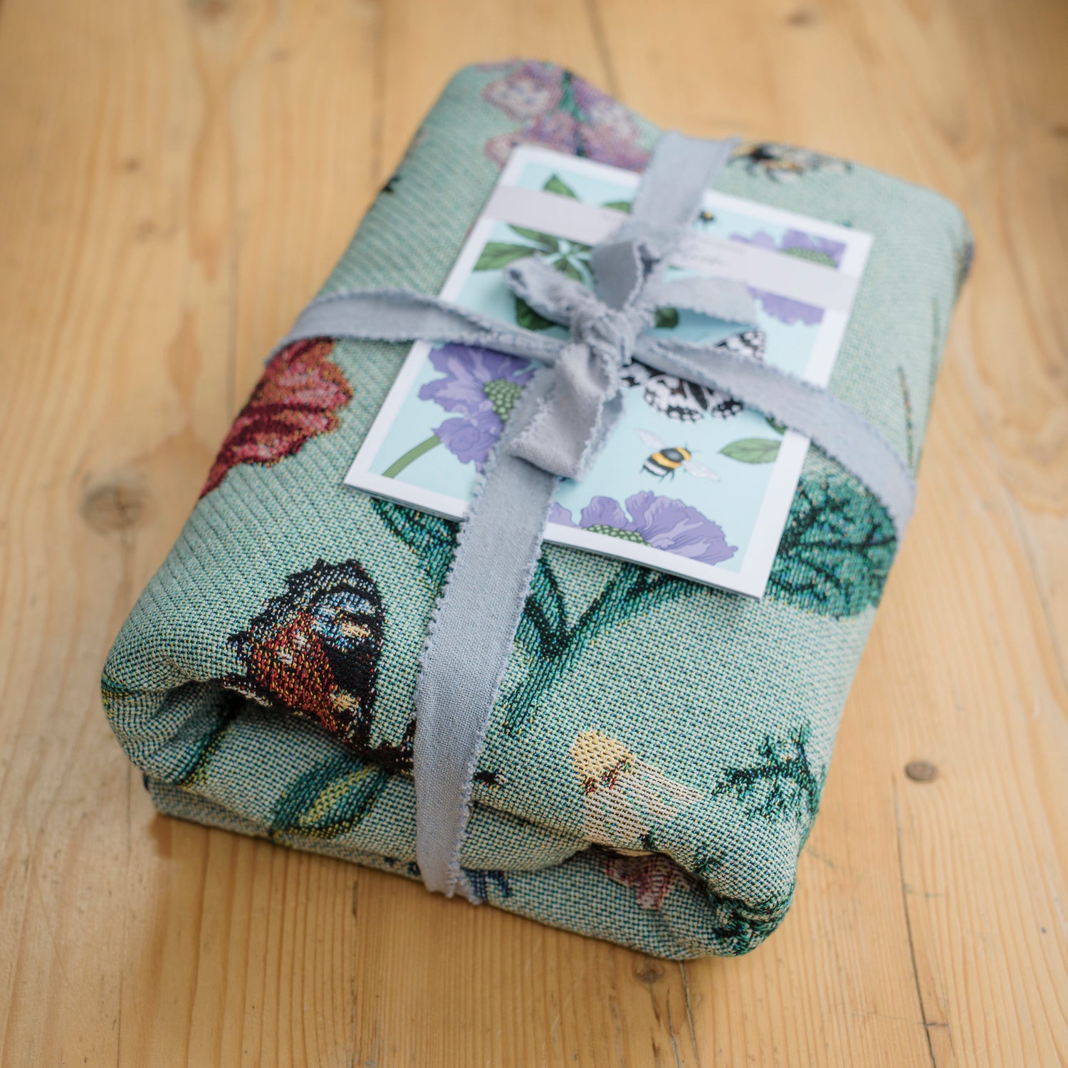 folded woven green blanket with butterfly and flower patterns tied with ribbon and guide book