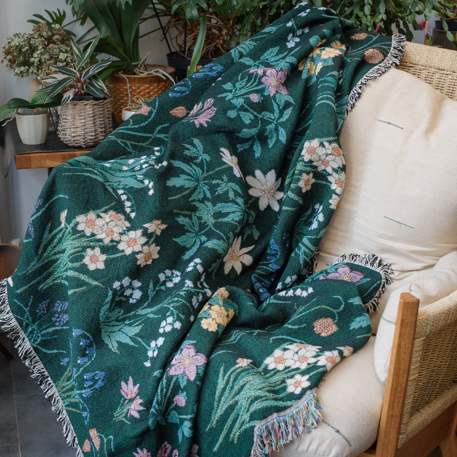 Spring flowers woven blanket in dark green with light coloured daffodils, forget me nots and bluebells spread across chair in home with houseplants
