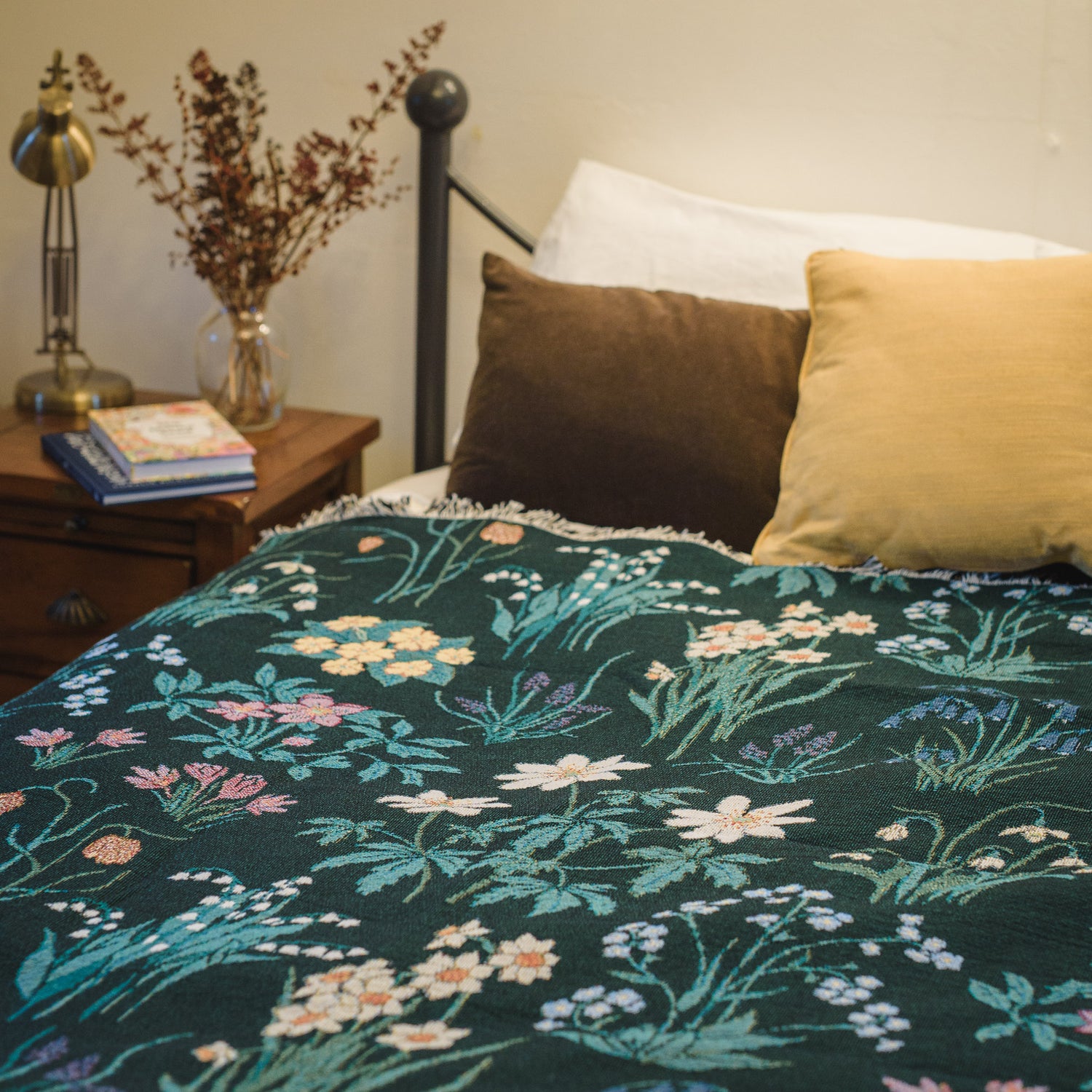Spring flowers woven blanket in dark green with light coloured daffodils, forget me nots and bluebells spread over bed