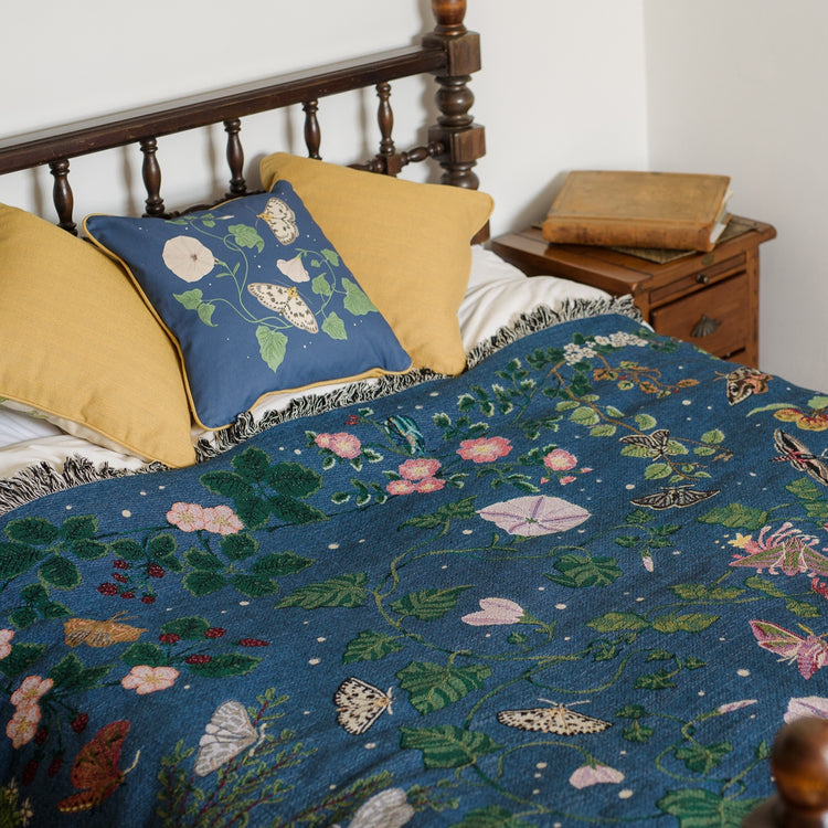 deep blue woven blanket with intricate moth and flower design spread across a double bed