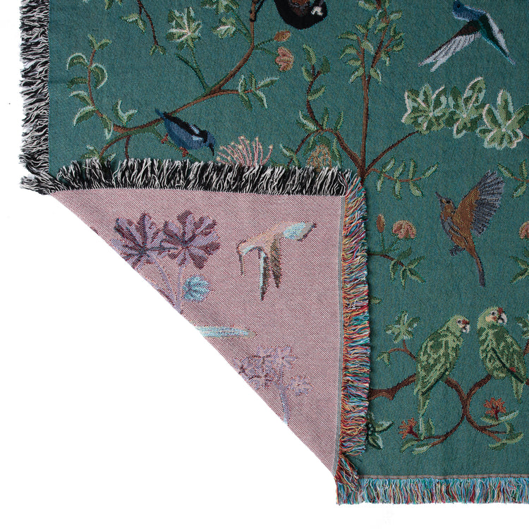 detial of teal green woven blanket showing purple reverse, featuring tropical birds