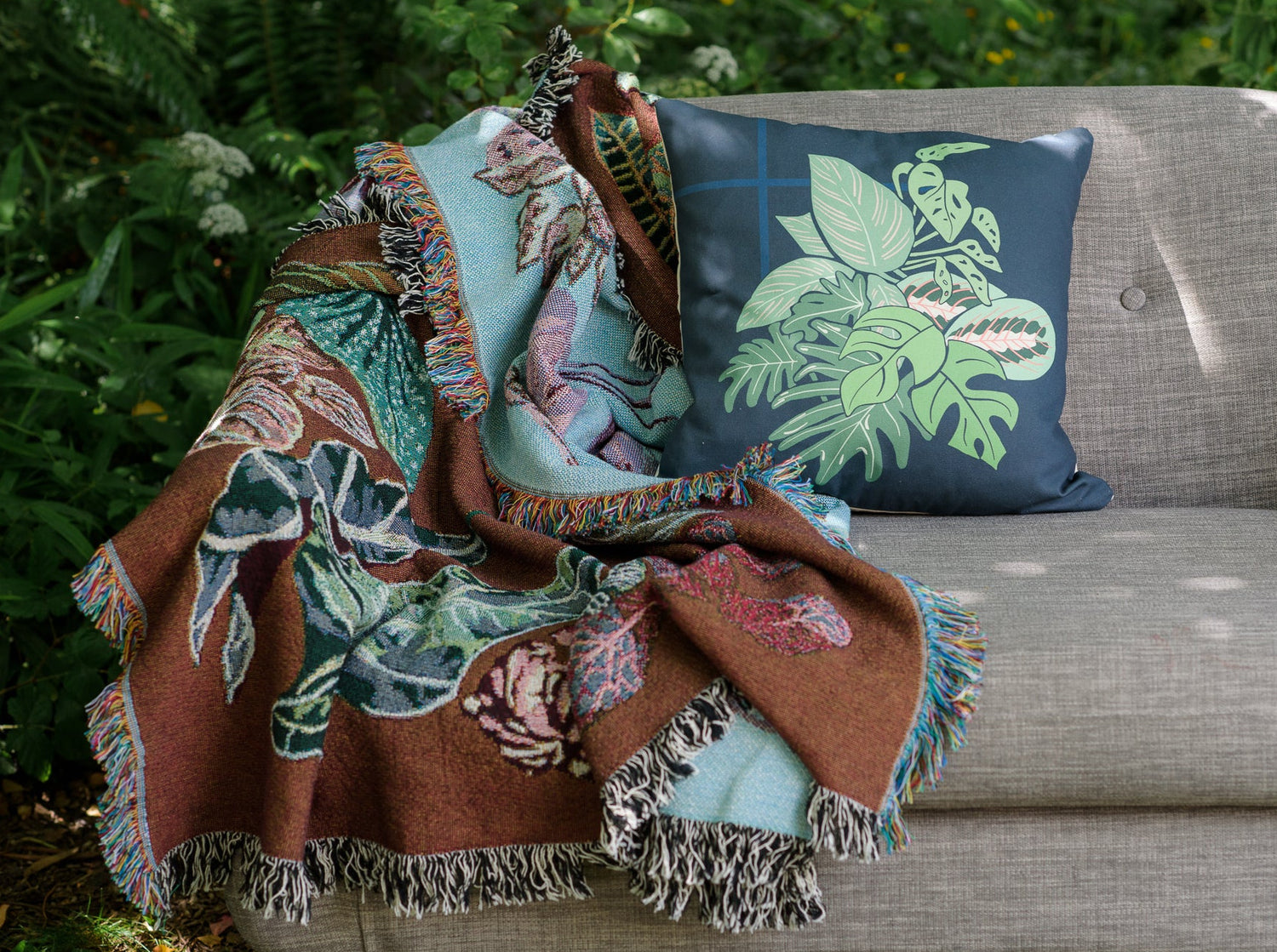 woven throw blanket in burgandy and light blue featuring houseplants on a sofa. 
