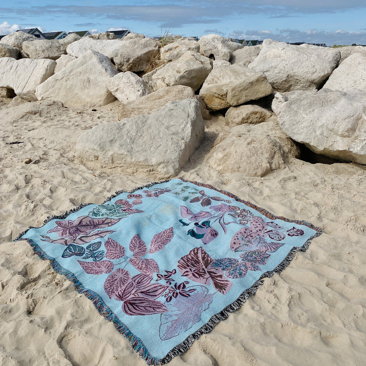 woven throw blanket featuring house plants in light blue and purple on the beach