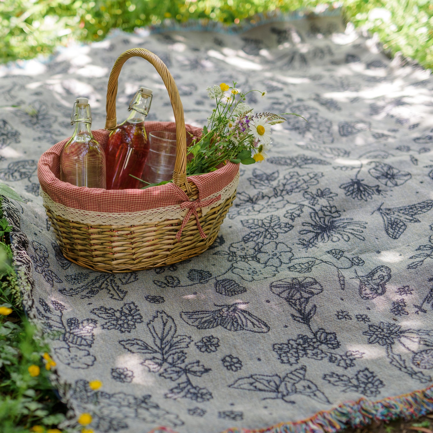 Pretty grey blanket with black pattern of moths, berries, leaves and flowers being usd as a picnic blanket