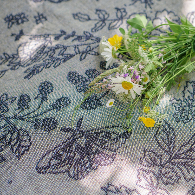 Pretty grey blanket with black pattern of moths, berries, leaves and flowers being used as a picnic blanket with a bunch of wildflowers