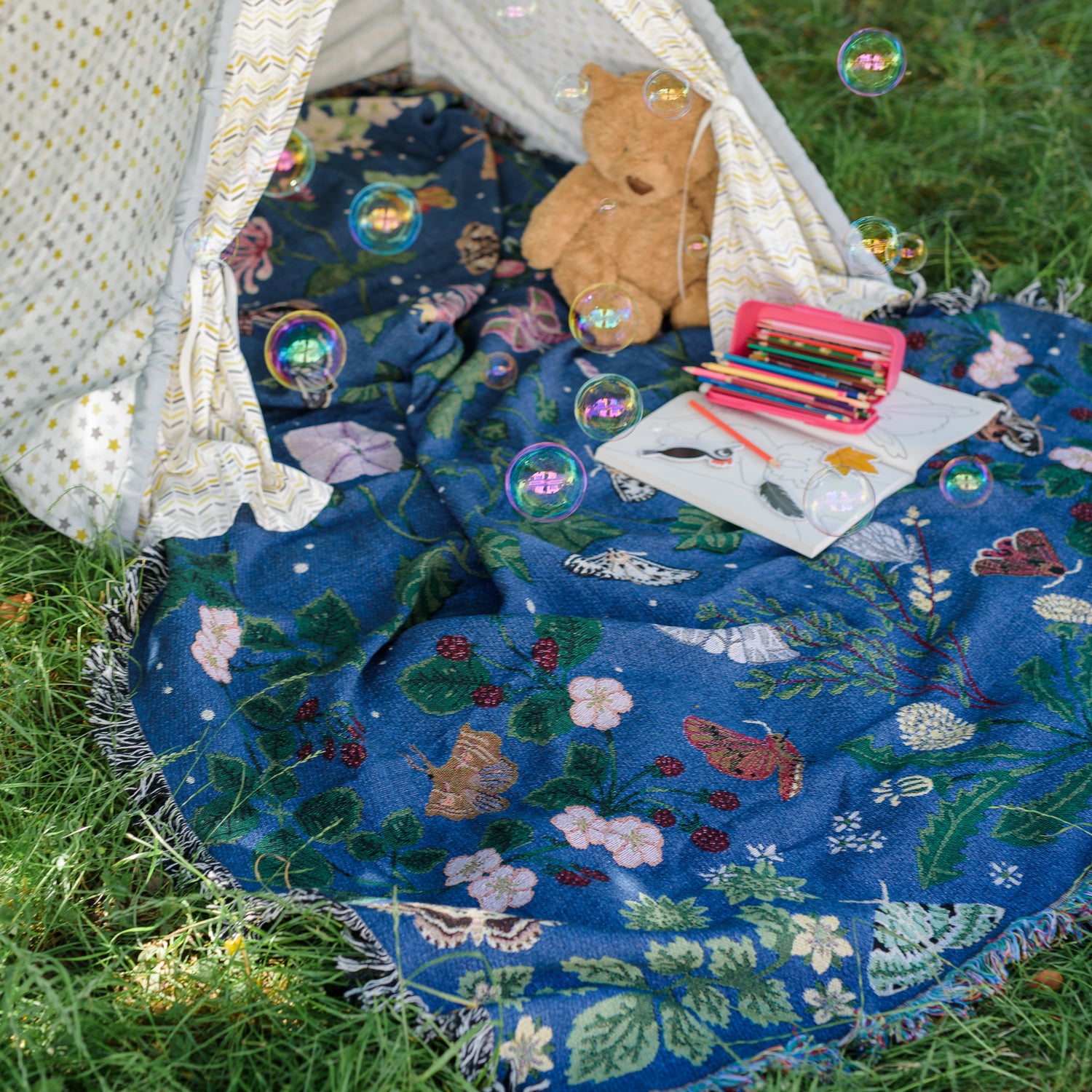 deep blue woven blanket with intricate moth and flower design being used as a magical picnic blanket with child&