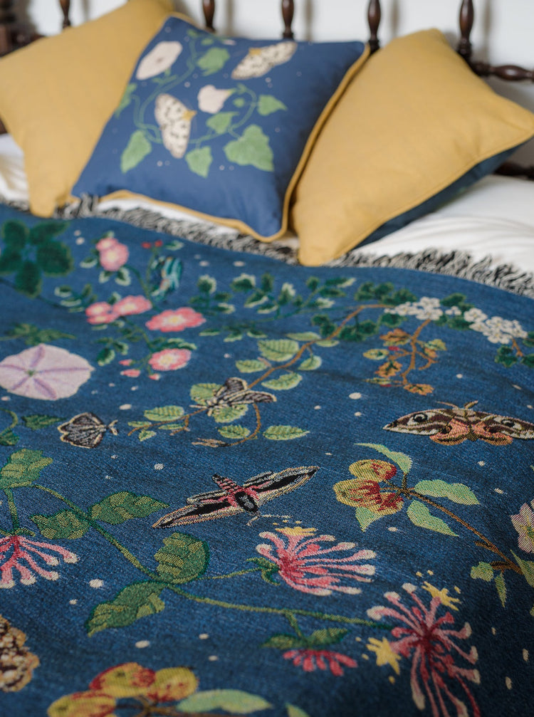 deep blue woven blanket with intricate moth and flower design spread on a bed