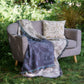 cream and blue two tone woven blanket featuring oak woodland butterfies and birds drapped across a sofa in garden