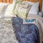 cream and blue two tone woven blanket featuring oak woodland butterfies and birds drapped across a bed