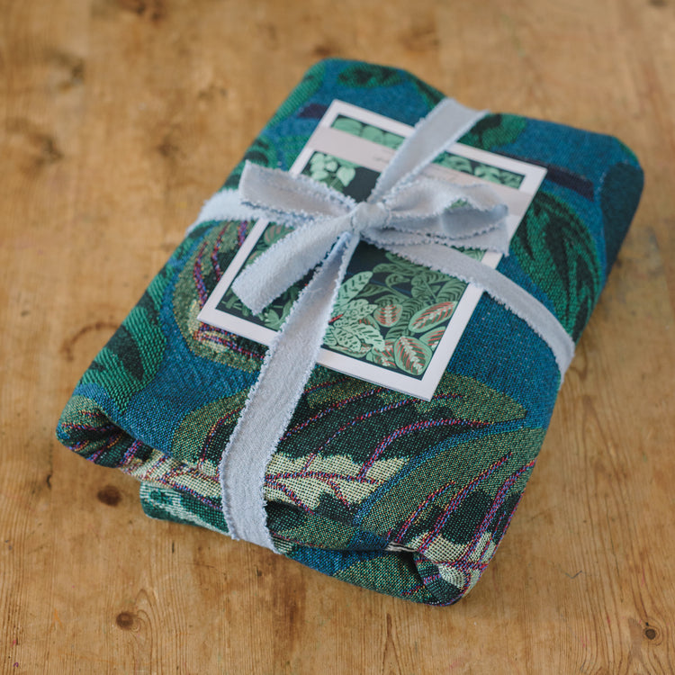 blue and green woven blanket featuring houseplants folded and tied with ribbon for the perfect gift