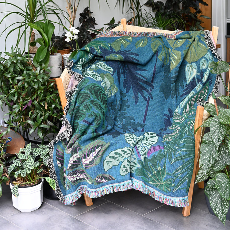 Teal and green woven blanket featuring houseplants in a airy living room with house plants all around