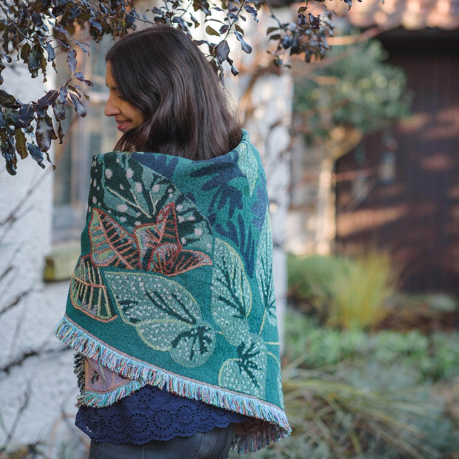 woven wrap blanket with fringe wrapped around womans shoulders in winter garden