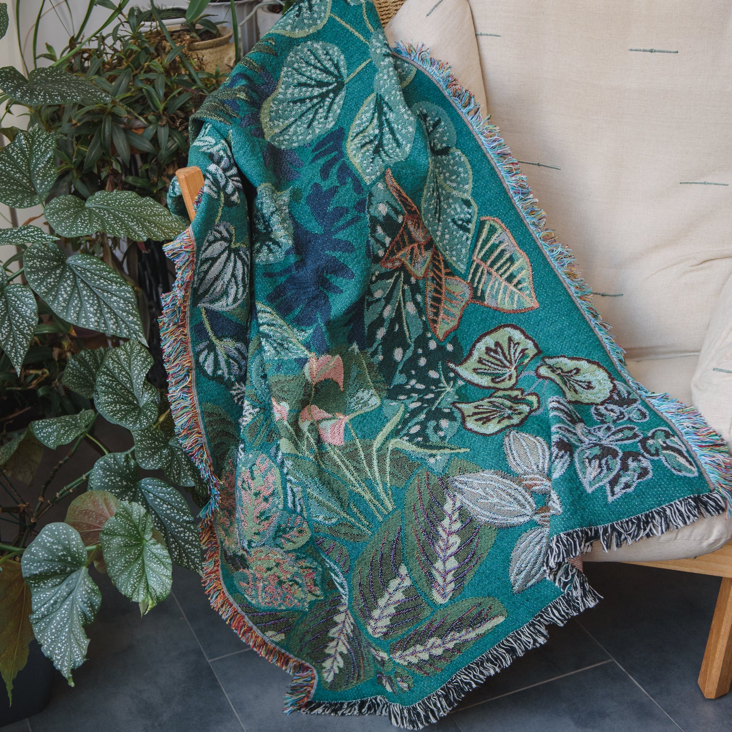 woven wrap blanket with fringe featuring lots of different houseplants draped over chair surrounded by houseplants