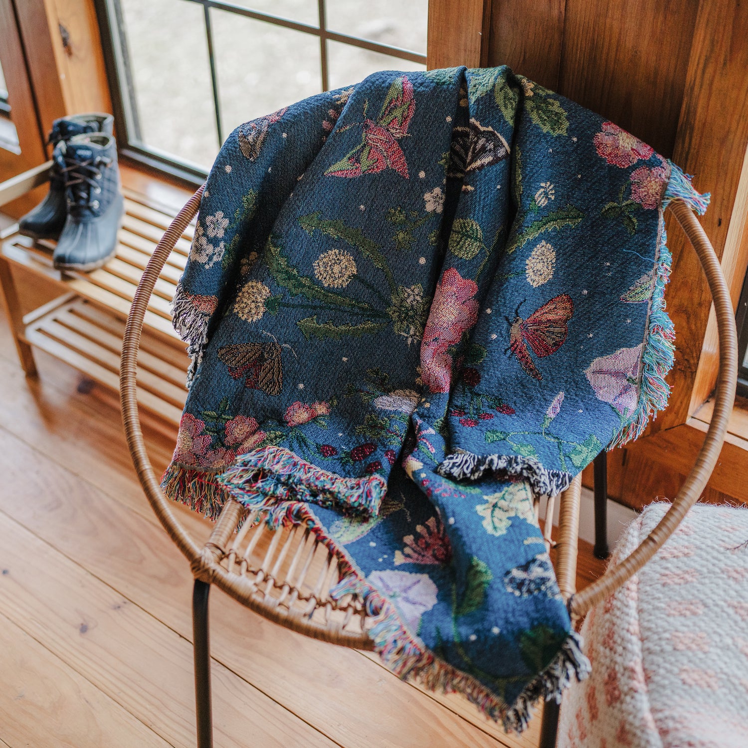 small dark blue woven wrap blanket with delicate moth and flower pattern over circular wicker chair in wood cabin