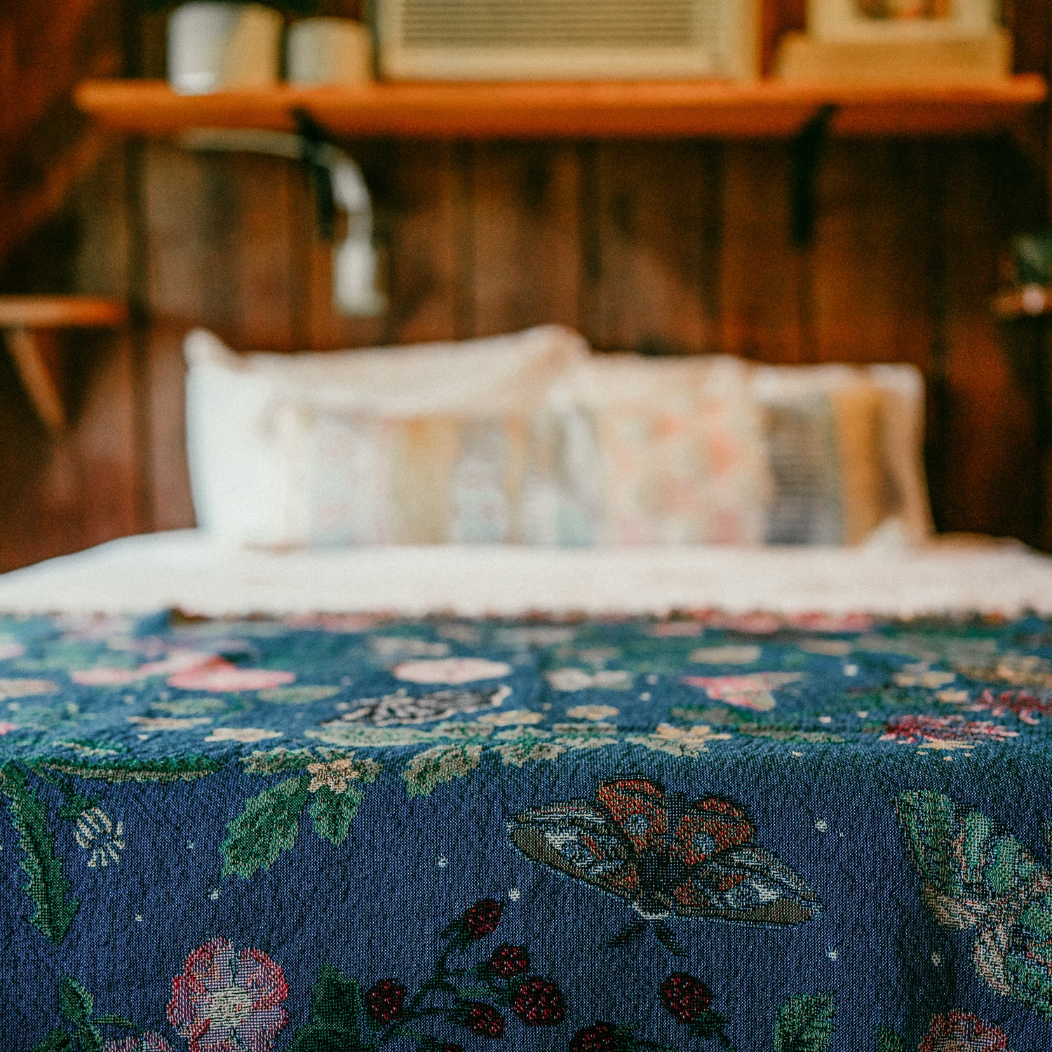 small dark blue woven wrap blanket with delicate moth and flower pattern across the bottom of a double bed in a wood cabin
