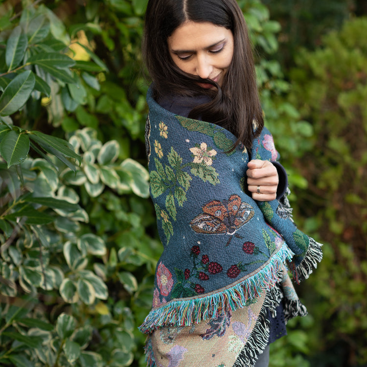 small dark blue woven wrap blanket with delicate moth and flower pattern around the shoulders of a woman in a garden