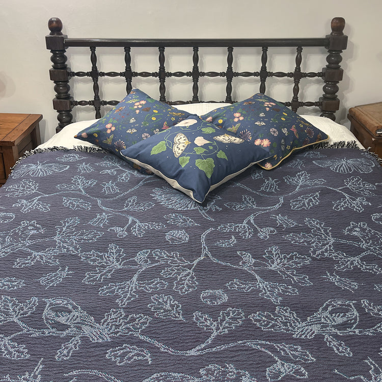  blue two tone woven blanket featuring oak woodland butterfies and birds spread across a bed