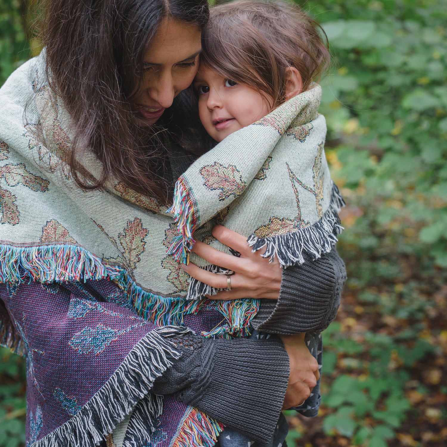 A woman holding a child in an Arcana Wild Oak Wrap Blanket.